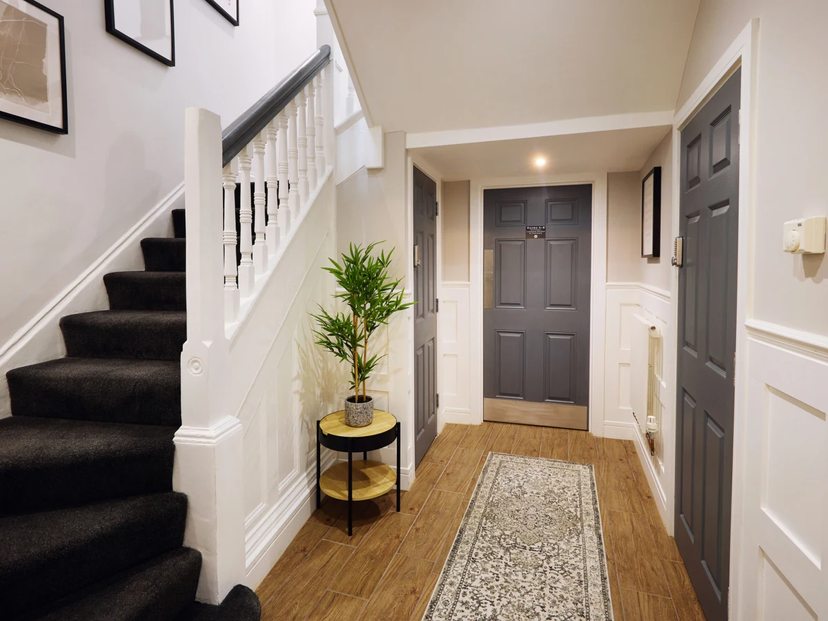 A finished hallway with white walls, a dark staircase carpet and a grey front door